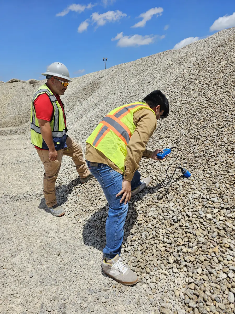 Two operators taking a portable moisture reading on the working face of an aggregate stockpile